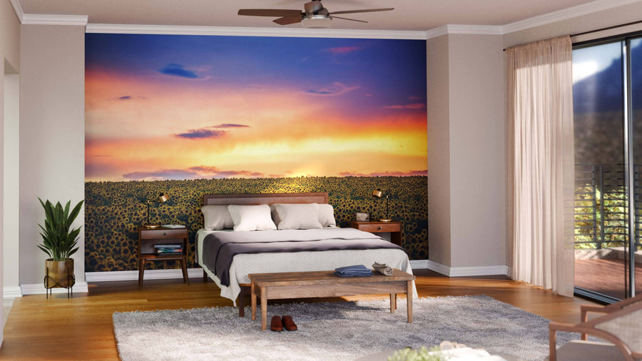 A modern bedroom features a bed with white and gray bedding, two wooden nightstands, and the Field of Blooming Sunflowers Wall Mural. A bench, a plant, and sheer-curtained windows complete the airy, warmly lit space.