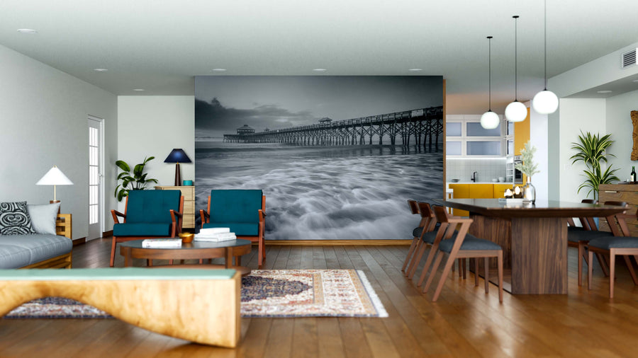 Modern open-plan living and dining area with wooden floors, blue and wood furniture, pendant lights, and a large Fishing Pier at Sunrise Wall Mural in black and white. The kitchen with yellow accents is visible in the background.