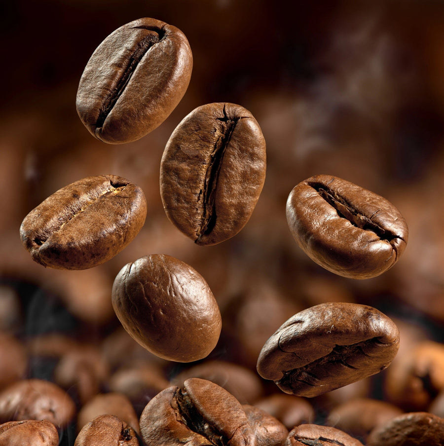 A modern cafe interior with wooden tables, stools, potted plants, large windows, pendant lights, and a bulletin board. The Floating Beans Wall Mural (peel and stick) covers one wall with images of floating coffee beans.