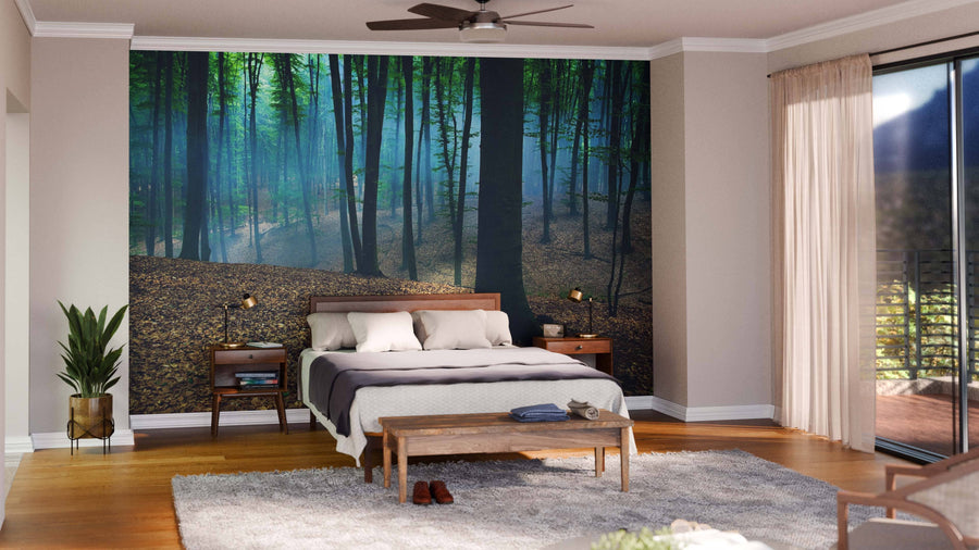 A cozy bedroom features a bed with white and gray bedding, wooden nightstands, a bench, and the Foggy Day in a Forest Wall Mural as an accent wall. A plant sits in the corner near sliding glass doors with beige curtains and a soft gray rug.