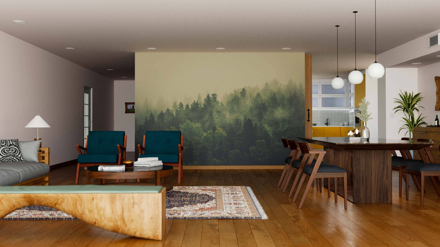 A modern living-dining room showcases wooden floors, a Foggy Forest Landscape Wall Mural, teal chairs, a wooden bench, gray sofa, round dining table with globe pendant lights, rugs, a visible kitchen area, and abundant natural light.