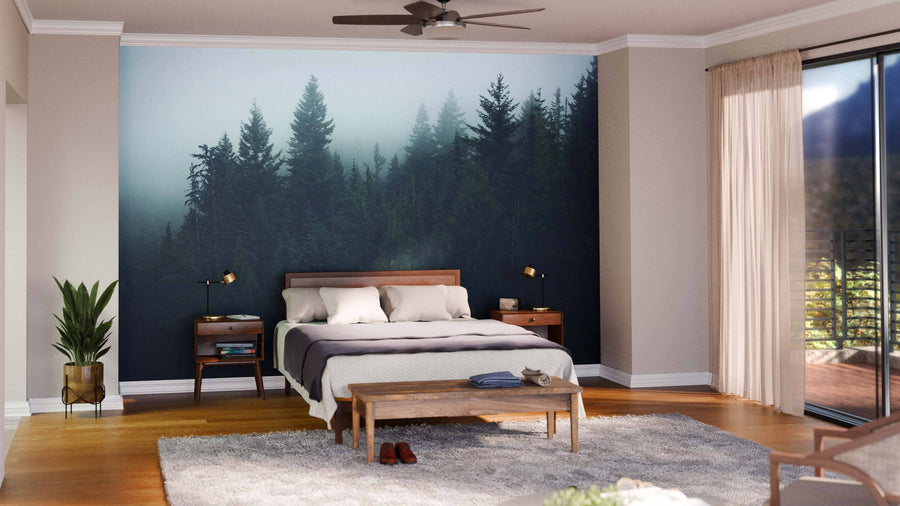 A modern bedroom features a Foggy Green Forest Wall Mural behind a wooden bed with white and gray bedding, two bedside tables with lamps, a bench at the foot of the bed, a green plant, gray rug, and floor-to-ceiling windows with sheer curtains.