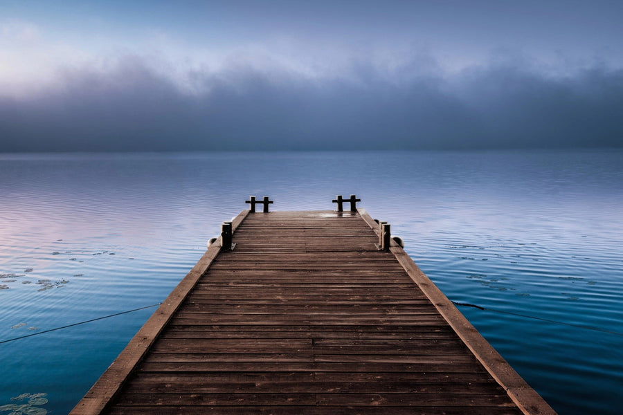 Modern living and dining area with wooden floors and stylish furniture; the Foggy Wooden Pier Wall Mural, featuring a dock over a calm blue lake beneath misty skies, adds a serene focal point to the open-concept space.