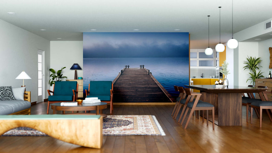 Modern living and dining area with wooden floors and stylish furniture; the Foggy Wooden Pier Wall Mural, featuring a dock over a calm blue lake beneath misty skies, adds a serene focal point to the open-concept space.