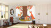 A bright nursery showcases the "Fox and Friends Wall Mural" with forest animals under autumn leaves. Sunlight streams in over a crib, rocking horse, plush rug, toy blocks, and a large white wardrobe.