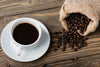 The Coffee 6 Wall Mural features a white cup of black coffee on a saucer, with dark roasted beans spilling from a burlap sack—ideal for adding fresh coffee vibes to your space with this custom printed wallpaper.