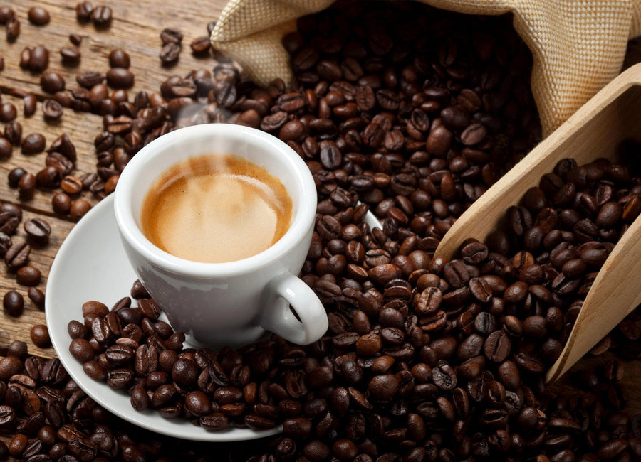 A modern coffee shop interior features wooden tables, black chairs, plants, hanging lights, and the Fresh Coffee Beans Wall Mural. Large windows along the left wall fill the cozy space with natural light.