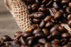Close-up of roasted coffee beans spilling from a sack onto wood, captured in detail for the Fresh Coffee Roast Wall Mural. The rich textures make this image perfect for peel and stick wall murals or removable wallpaper.