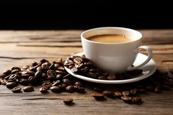 A white ceramic cup of coffee sits on a matching saucer on a wooden table, surrounded by scattered coffee beans. This rustic scene echoes the charm of the "Coffee 6 Wall Mural". The dark background enhances its contrast and warmth.