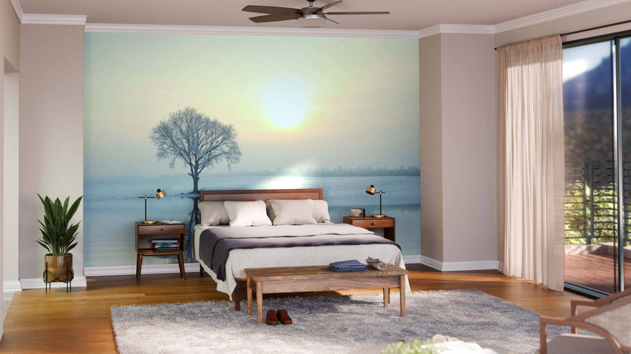 A modern bedroom features a wood bed, side tables, lamps, and the Frosted Tree at Sunrise Wall Mural. Sunlight streams in through sheer curtains. A gray rug, plants, and a wooden bench complete the cozy decor.