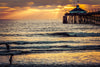 Transform your space with the Golden Coast Horizon Wall Mural, featuring a dramatic ocean sunset with golden rays and a pier reaching into the water. Available as a custom printed mural or removable wallpaper.