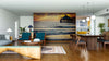Modern open-plan living and dining area with wooden floors, teal and wood furniture, pendant lights, and the Golden Coast Horizon Wall Mural depicting a sunset over the ocean with a pier. Area rugs and decor add cozy style.
