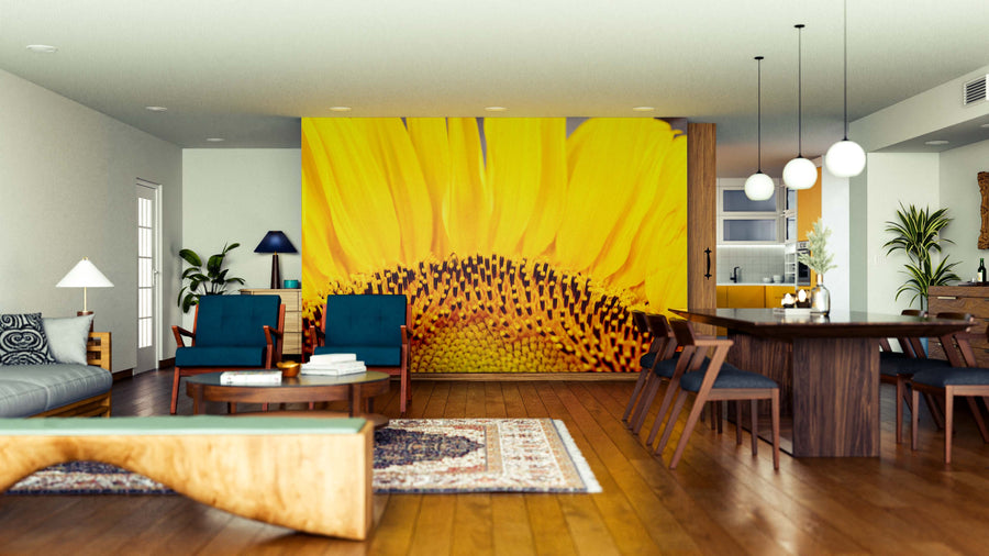 A modern living-dining room with wooden floors and mid-century furnishings features the Golden Petal Wall Mural—a vibrant yellow sunflower design—alongside pendant lights, mixed blue and wood chairs, green plants, and patterned rugs.
