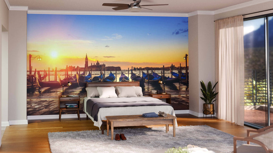 A modern living and dining room with wooden floors and stylish furniture features the Gondolas Wall Mural, a peel and stick artwork of Venetian gondolas at sunset, bringing warmth and vibrant color to the elegant, open space.