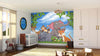 A bright nursery with wooden floors, crib, and large wardrobe features the Happy Wild Bunch Wall Mural—cartoon jungle animals amid grass and leafy branches under a blue sky. A toy rocking horse and other toys are on the floor.