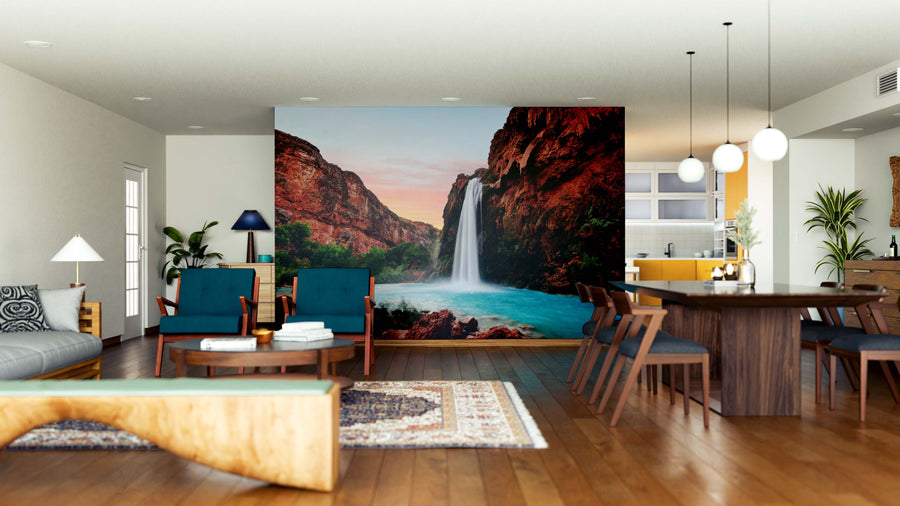 Modern open-concept living and dining area with wood floors and stylish furniture. A large Havasu Falls Sunset Wall Mural adds vibrant color as the room’s focal point. Pendant lights hang above the dining table; kitchen is visible in the background.