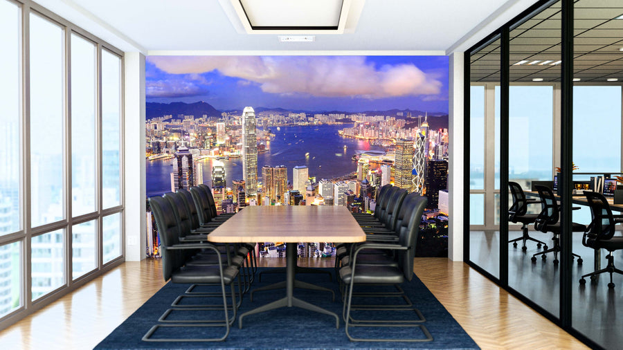 A modern conference room with a long wooden table, black chairs, and a blue rug. The back wall displays the Hong Kong Central District Skyline Wall Mural, showing skyscrapers and city lights. Glass walls separate adjacent offices.