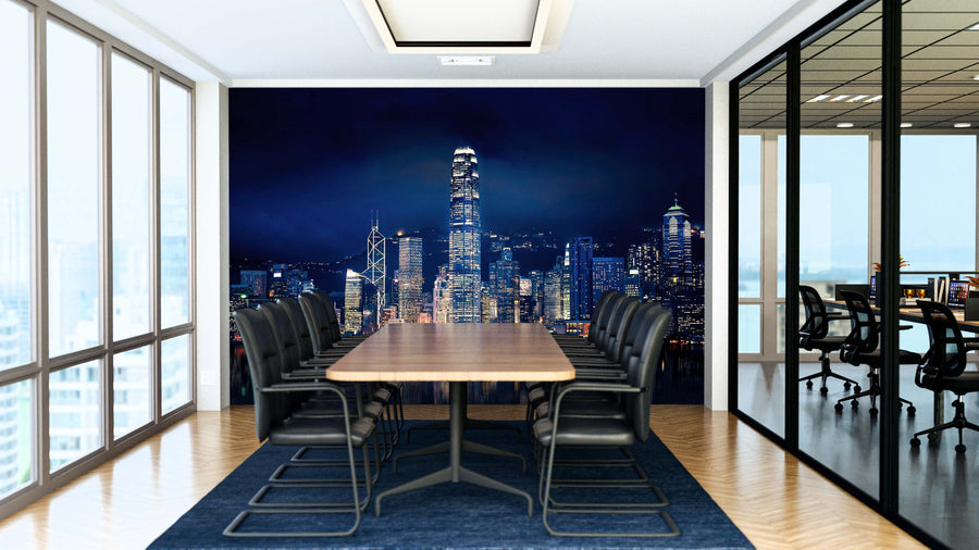 A modern conference room features a long wooden table, black chairs, and a blue rug. One wall displays the Hong Kong Lights Wall Mural depicting a city skyline at night. Glass walls reveal another office with a similar setup.