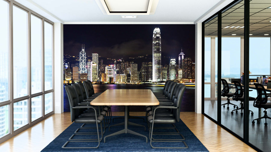 A modern conference room features a long wooden table, black chairs, floor-to-ceiling windows, glass walls, and a Hong Kong Skyline Wall Mural on the back wall. Another office space is visible through the glass wall.