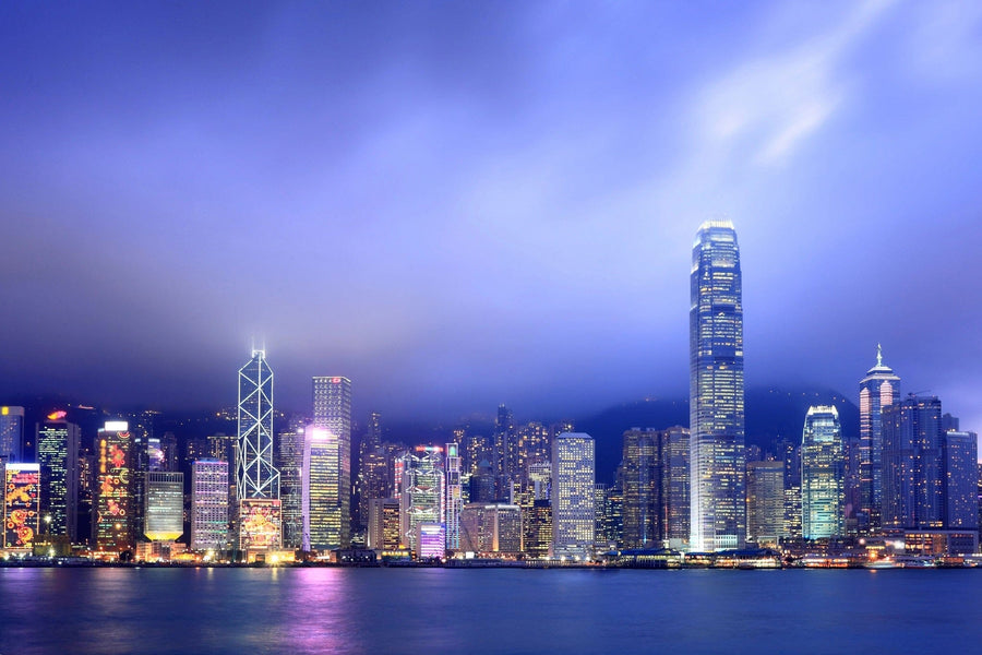 A modern conference room with a long table, black chairs, and glass walls. The far wall displays the Hong Kong at Night Wall Mural, featuring illuminated skyscrapers at dusk. Adjacent room is visible through the glass partition.