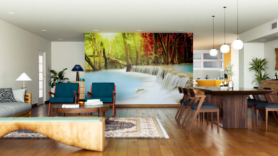 A modern open-plan living and dining area with wood floors, teal chairs, and a large table features the Huai Mae Kamin Waterfall Wall Mural. Plants and mid-century furniture complete this bright, airy space.