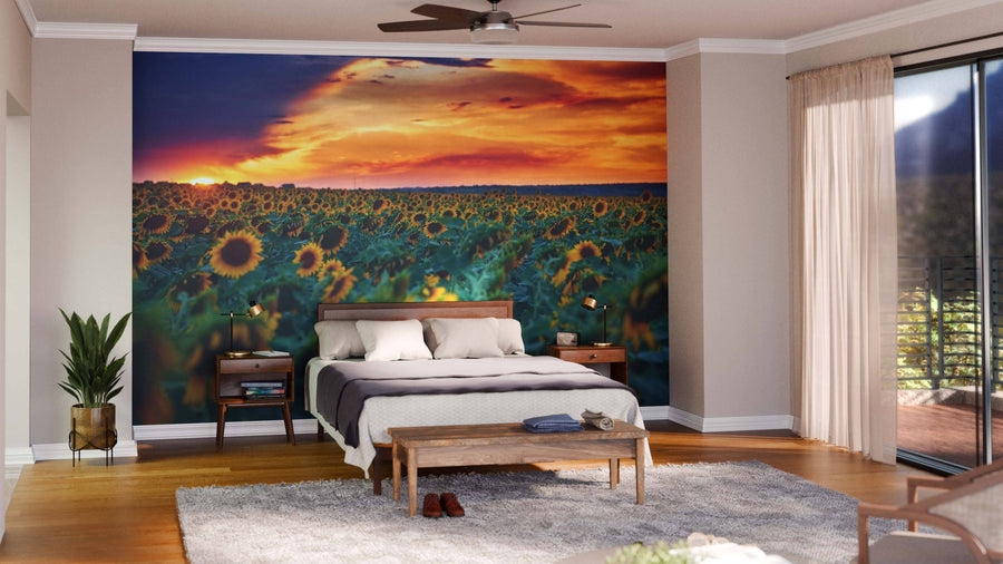 Modern open-concept living and dining area features wood floors, green and wood furniture, and an Illuminated Sunflower Field Wall Mural peel-and-stick at sunset. Pendant lights hang above the table; kitchen is visible in the background.