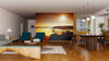 A modern living-dining room has wood floors, a gray sofa, teal armchairs, a wood dining set, and the Above the Clouds Wall Mural depicting a person on a cliff at sunrise. Pendant lights illuminate the dining table and a rug accents the seating area.