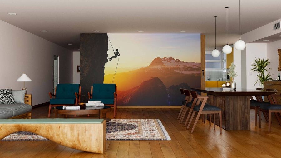 A modern living-dining room with wooden floors, stylish furniture, and the "Ascent of Courage Wall Mural" depicting a rock climber at sunset with mountain scenery. Warm lighting and contemporary decor complete the space.
