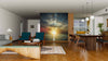 A modern, open-plan living and dining room with wooden floors, blue and wood furniture, pendant lights, and the Asphalt Road and Sunset Wall Mural as a striking peel-and-stick accent. The kitchen area appears in the background.