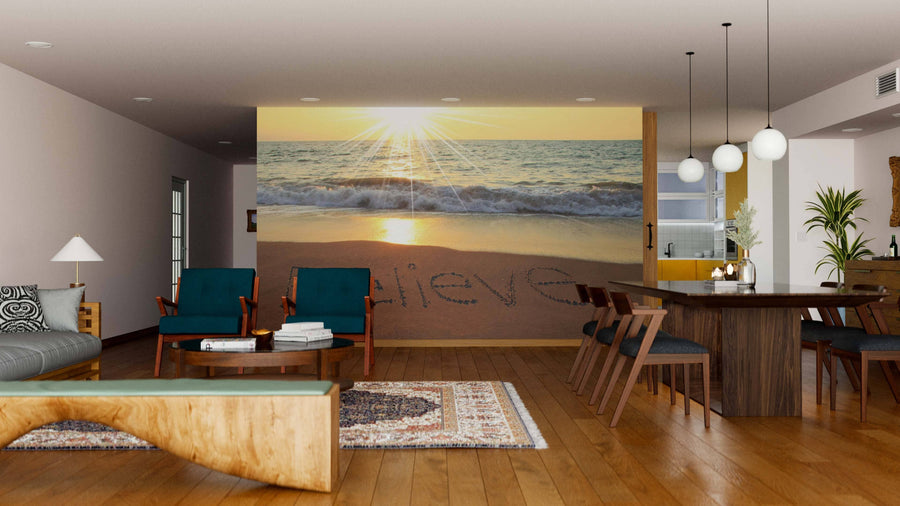 A modern living-dining area with wooden floors and mid-century furniture features the Believe Wall Mural, displaying a beach sunrise with "believe" in the sand. Sunlight fills the space, adding warmth and inviting charm.