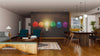 Modern living-dining room with wooden floors, teal armchairs, and a rug. The back wall showcases the Bright Idea Wall Mural—crumpled rainbow paper balls and a glowing lightbulb above the wooden dining table.
