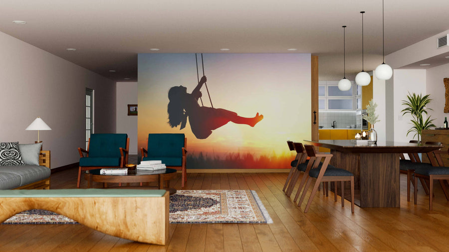 A contemporary living-dining space with wood floors and mid-century furniture features the “Child on Swing Wall Mural” at sunset, plus a wooden dining table, green chairs, pendant lights, rugs, and an open kitchen in the background.
