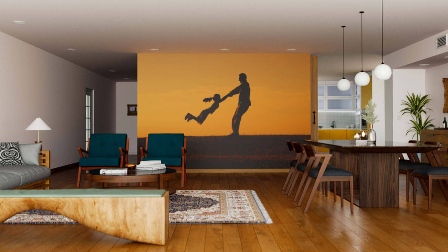A modern living-dining area with wood floors and stylish furniture features the "Father and Daughter Wall Mural," which shows a silhouette of an adult swinging a child against an orange sunset, adding warmth and playfulness to the decor.