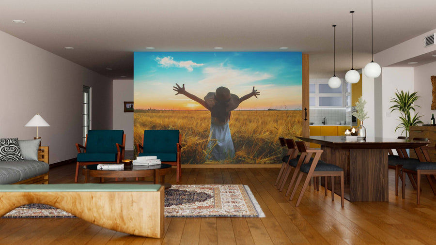 A modern living-dining area with wood floors, teal armchairs, and a rustic coffee table. The "Fields of Freedom Wall Mural" adds vibrant sunset hues to the neutral space, complemented by pendant lights above the dining table.