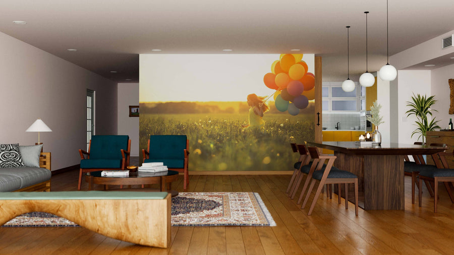 Modern open living-dining area with wood floors, teal chairs, patterned rug, wooden dining table, and globe lights. The back wall features the Girl with Balloons Wall Mural depicting a child in a field holding colorful balloons at sunset.