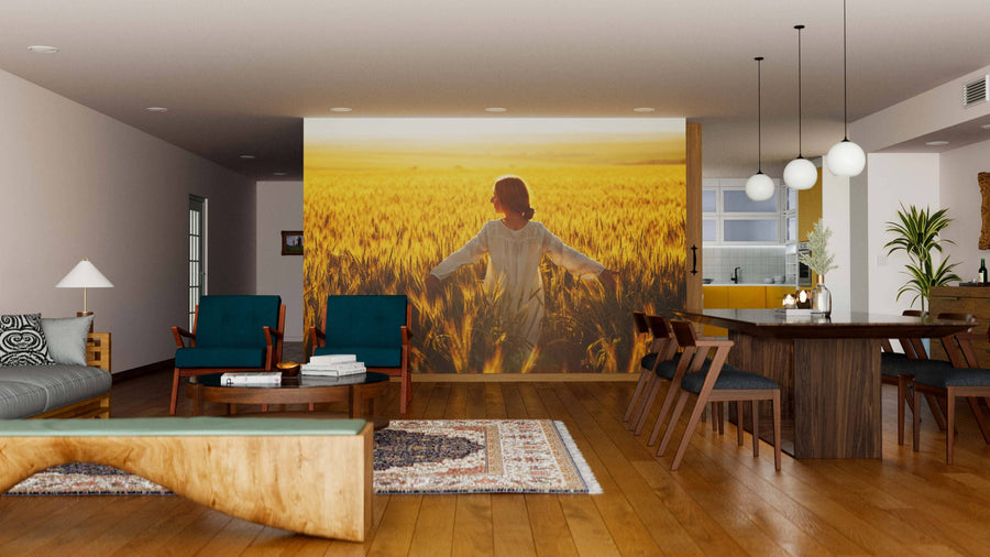 Modern living-dining room with wooden floors, mid-century furnishings, teal chairs, and natural decor. A large Golden Serenity Wall Mural shows a person standing in a wheat field at sunset, adding warmth to the inviting space.