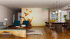 A modern open living-dining space with wood floors, mid-century furniture, a green sofa, blue chairs, patterned rugs, globe lights, a yellow kitchen in the background, and the Golden Sky Wall Mural showing silhouettes of a child releasing birds.
