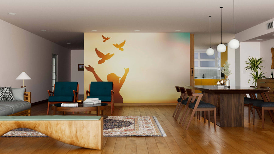 A modern open living-dining space with wood floors, mid-century furniture, a green sofa, blue chairs, patterned rugs, globe lights, a yellow kitchen in the background, and the Golden Sky Wall Mural showing silhouettes of a child releasing birds.