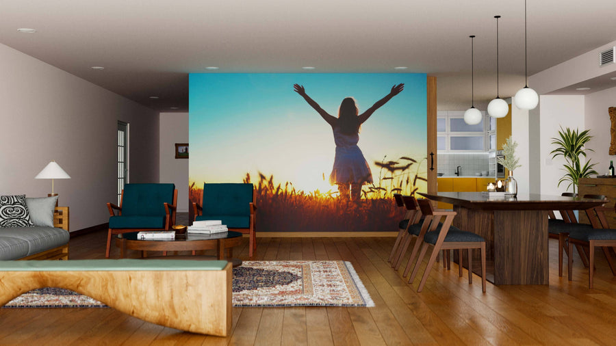 A modern living-dining room with wood floors, teal chairs, and the Harvest Glow Wall Mural depicting a person at sunset. Features include a wooden table, stylish lighting, and cozy artistic decor for an inviting atmosphere.