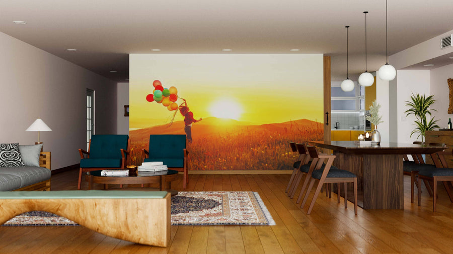 A modern living and dining room with wooden floors, blue chairs, and a large Joyful Sunset Freedom Wall Mural of a child with balloons at sunset creates a warm atmosphere. Spherical pendant lights hang above the dining table.