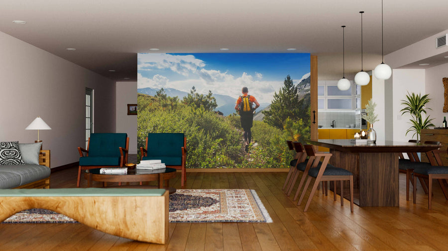 A modern living-dining area with wood floors, stylish furniture, and pendant lights features the Mountain Trail Adventure Wall Mural—showing a hiker amid lush greenery and a bright sky to bring nature into the space.