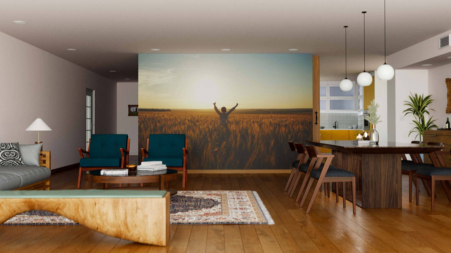 A modern living-dining room with wood floors, teal chairs, and a unique coffee table features the Standing in Wheat Field Wall Mural. Pendant lights, a cozy rug, and plants complete the look.