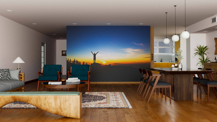 Modern living-dining room with wood floors, green chairs, and the Sunrise Triumph Wall Mural featuring a person on a mountaintop at sunrise. The mural adds color and depth to the open space with its wooden dining set and contemporary lighting.