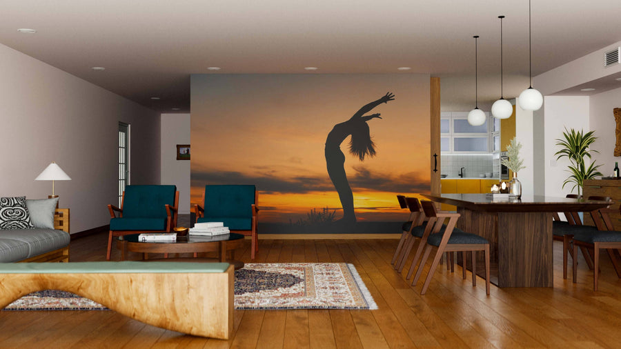 A modern living-dining room with wood floors, teal armchairs, and pendant lights is enhanced by the Sunset Serenity Wall Mural—its striking silhouette at sunset brings style and warmth to the contemporary decor.