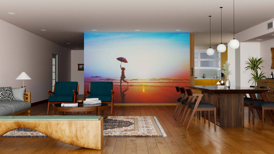A modern living-dining room with wood flooring and mid-century furniture. A feature wall showcases the Sunset Stroll Wall Mural, displaying a person walking on a beach at sunset, bringing vibrant color to the neutral interior.