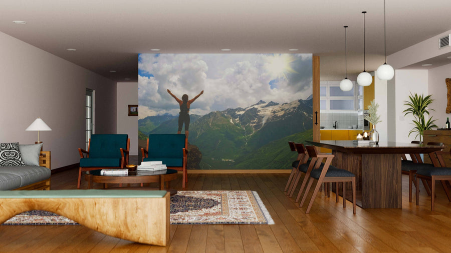 A modern living-dining room with wooden floors and mid-century furniture features the Top of the Mountain Wall Mural—a custom print of a person overlooking mountains, seamlessly bringing nature and sunlight into the space.