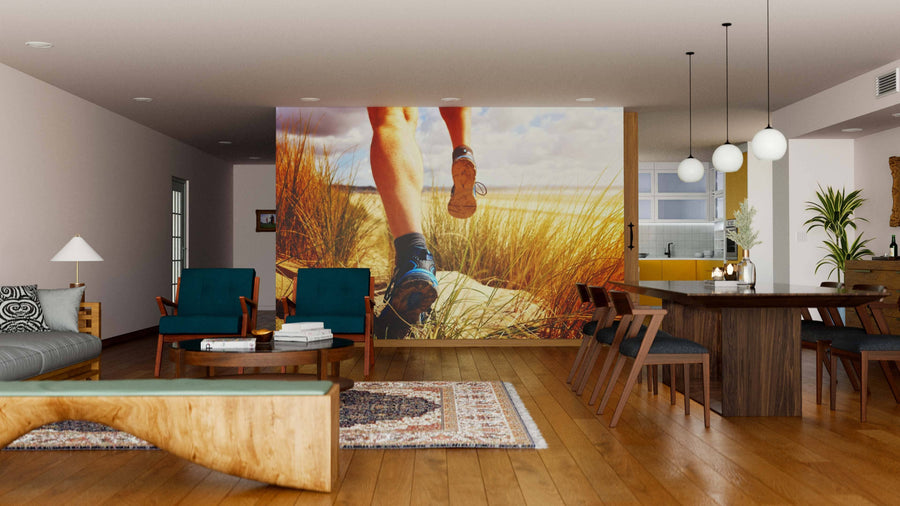 A modern living-dining room with wooden floors, green armchairs, and round pendant lights features the Trailblazing Steps Wall Mural of running legs through grass on the back wall, creating a dynamic, outdoorsy vibe in the cozy space.