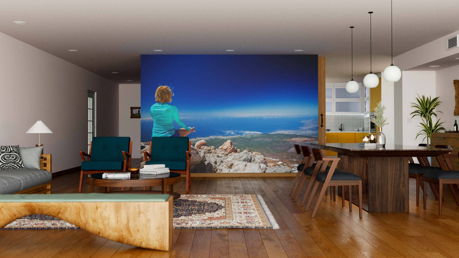 A modern living-dining room with wood floors, dark chairs, a rug, and a unique bench features the “Woman Doing Yoga Wall Mural,” depicting someone on a mountain and bringing an open, serene atmosphere to the space.