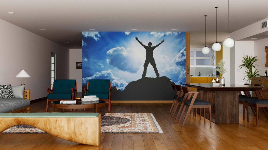 A modern living-dining room features the Worship Wall Mural of a triumphant person on a mountain peak, wooden floors, a dining table with chairs, armchairs, a sofa, and contemporary lighting.