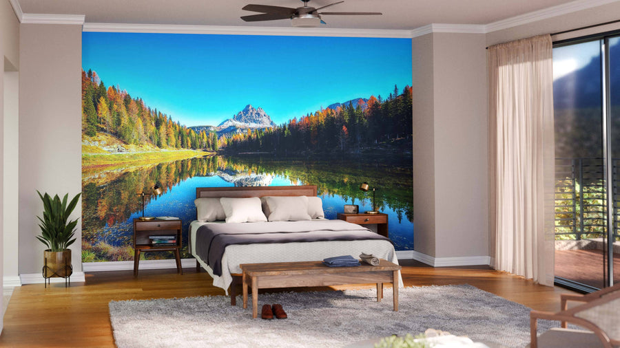 A modern living-dining room features wood floors, stylish furniture, and a striking Lake Antorno & Dolomite Peak Wall Mural. Pendant lights hang over the dining table while natural light streams in from the windows.